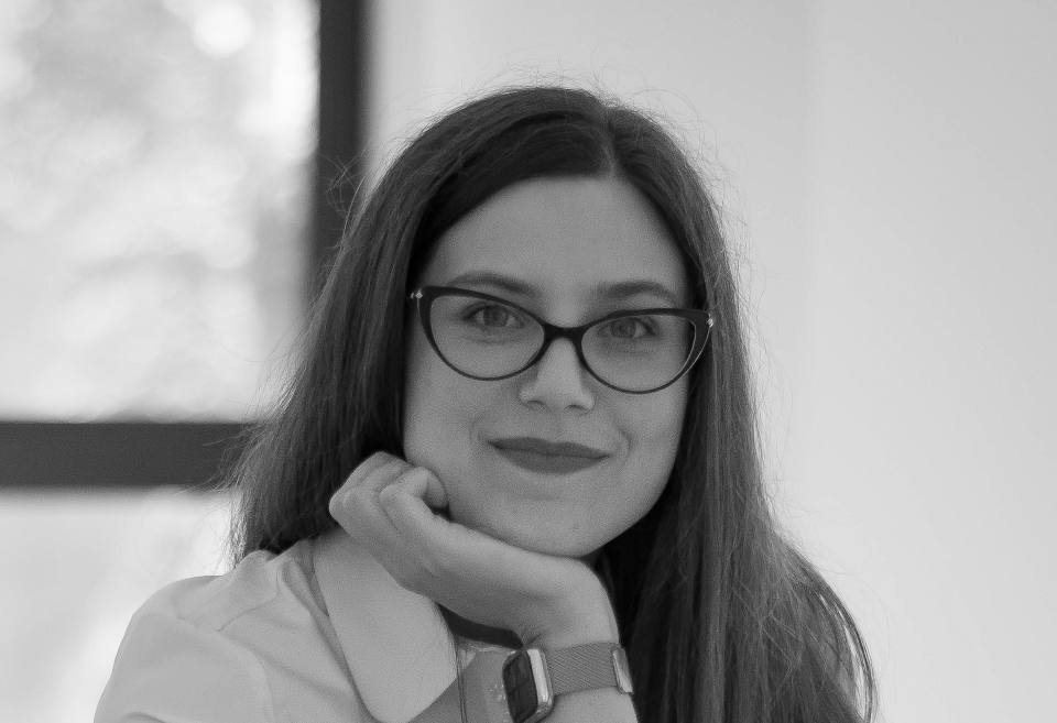 Tina Jura sprijinindu-și bărbia în mână, lângă o fereastră mare.